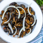 Cameroonian snails on a white plate topped with sliced onions.