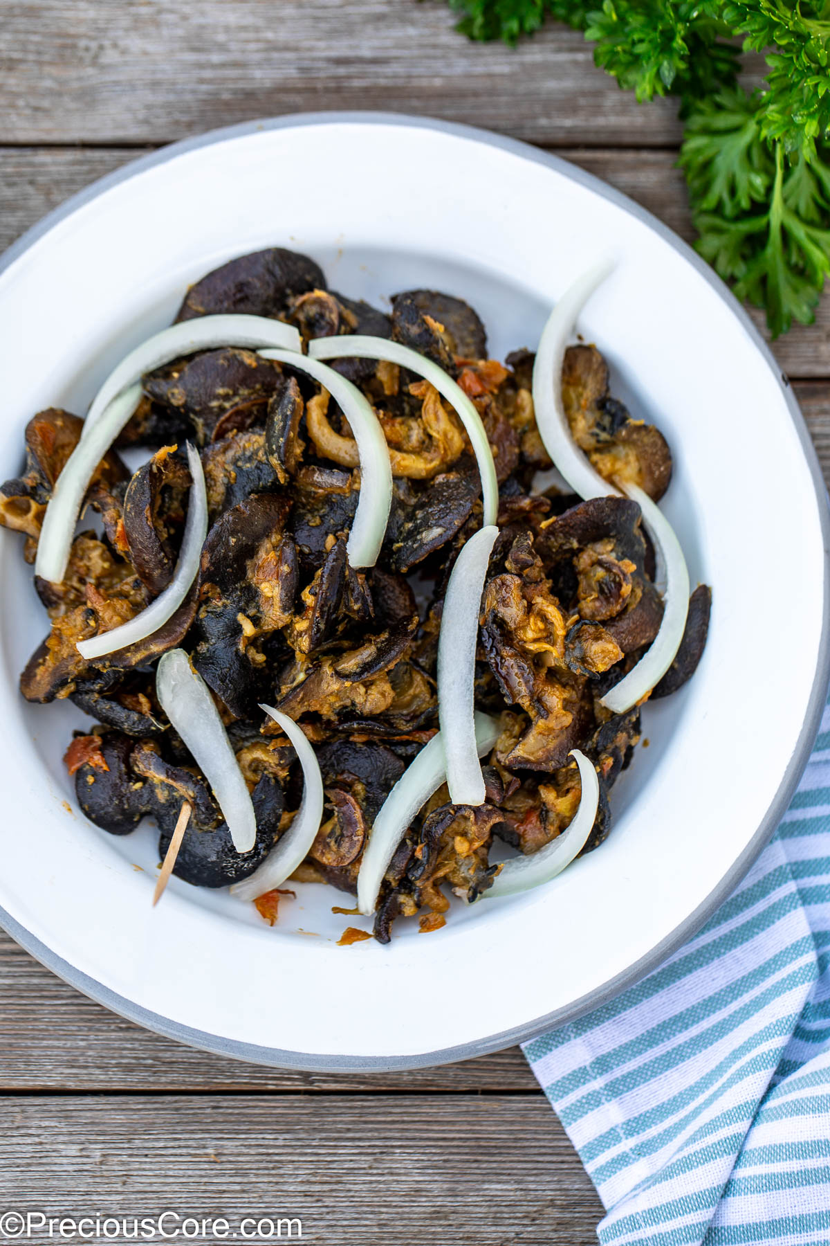 Cameroonian snails on a white plate topped with sliced onions.