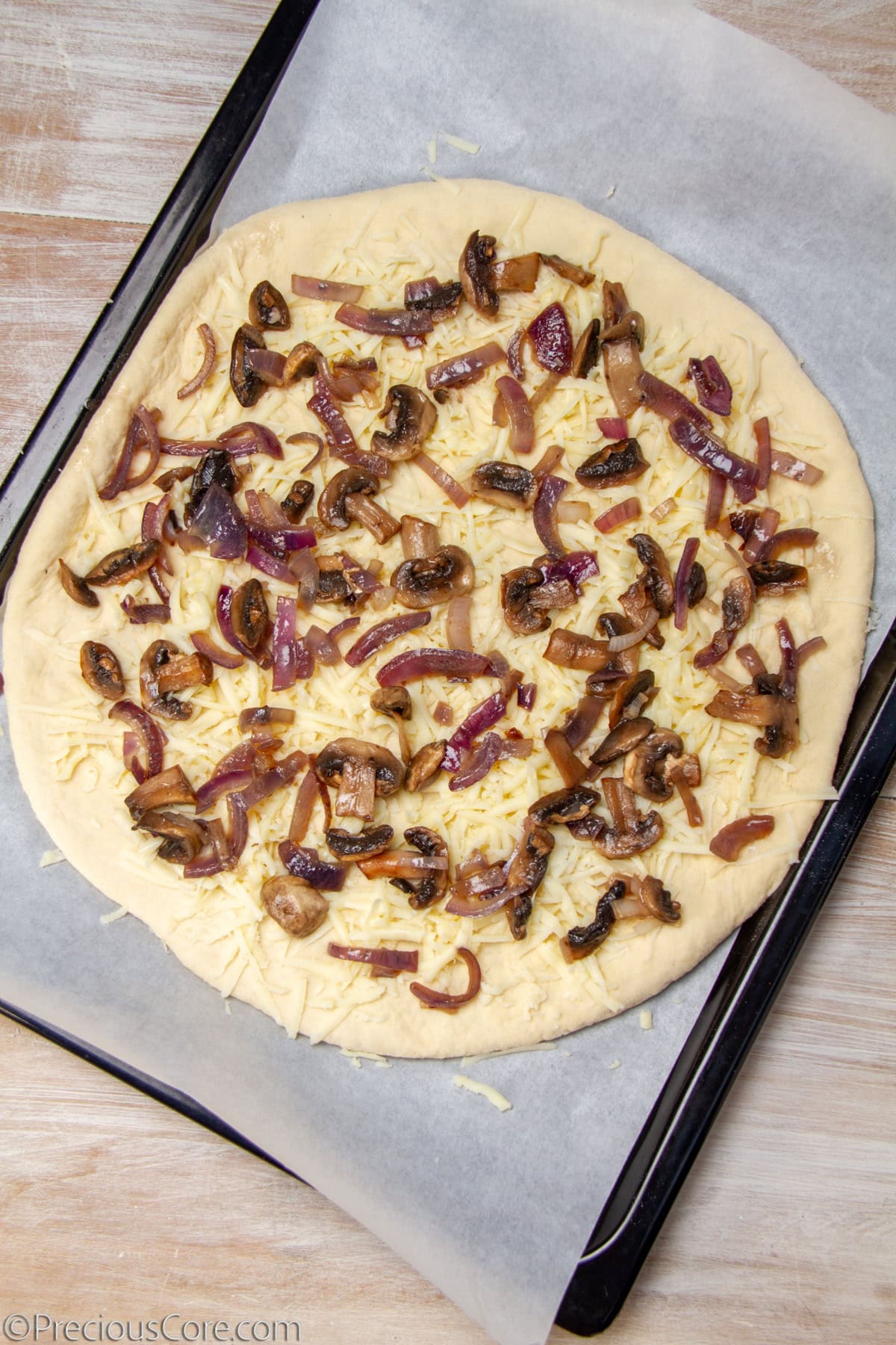 Uncooked pizza topped with mushrooms, cheese, and caramelized onions.