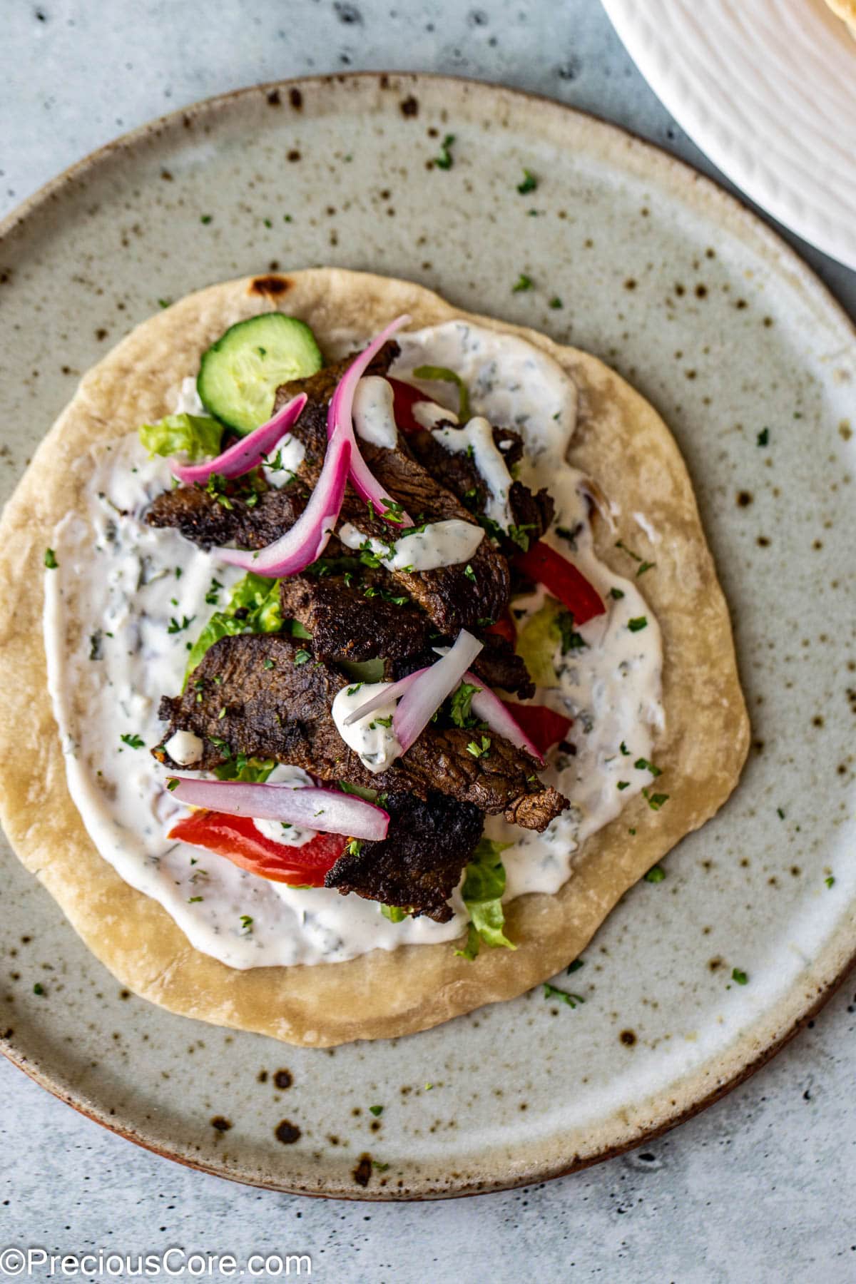 A flatbread topped with beef shawarma, veggies, and sauce.