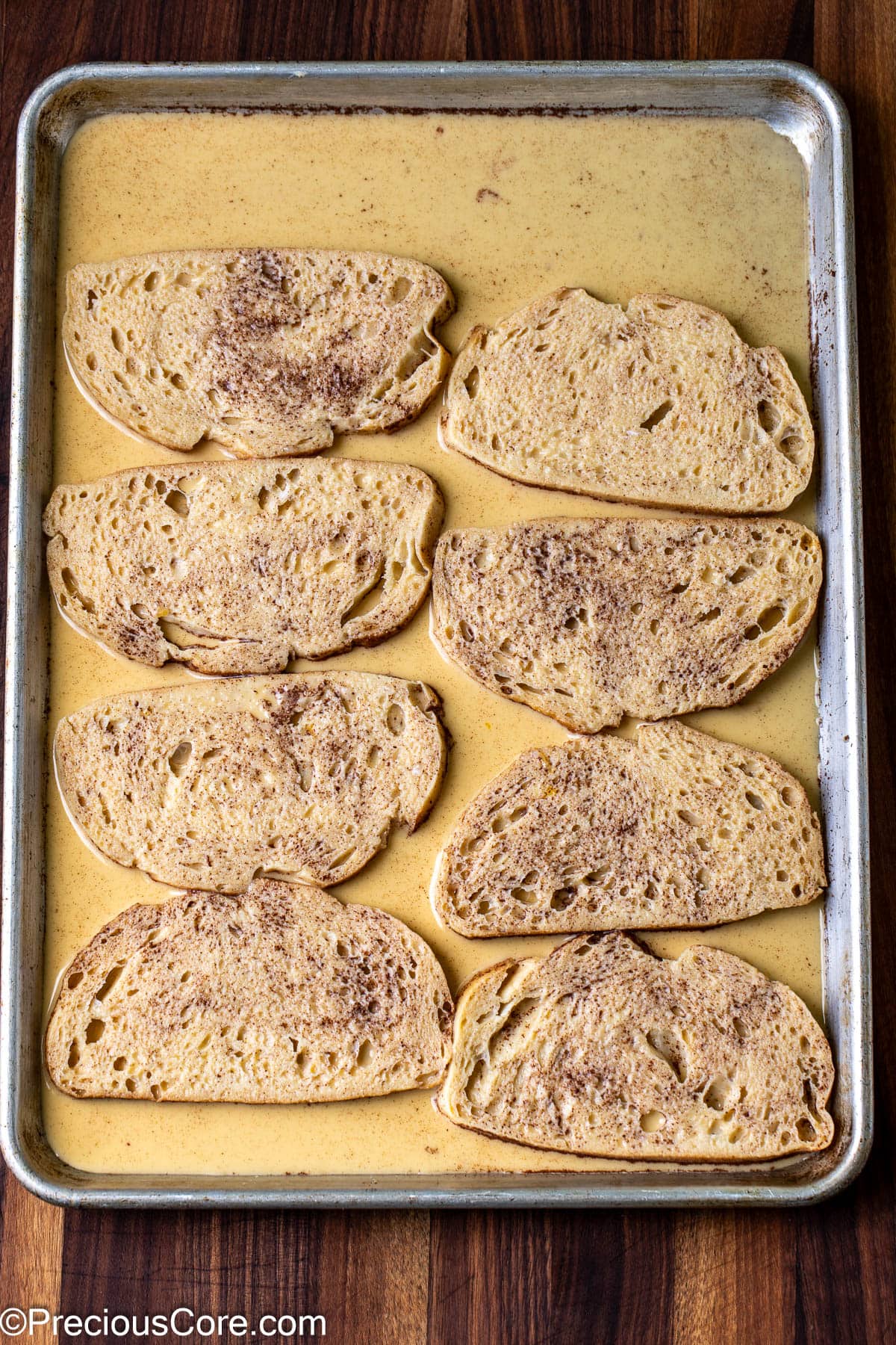 Bread slices soaking in custard on a baking sheet.