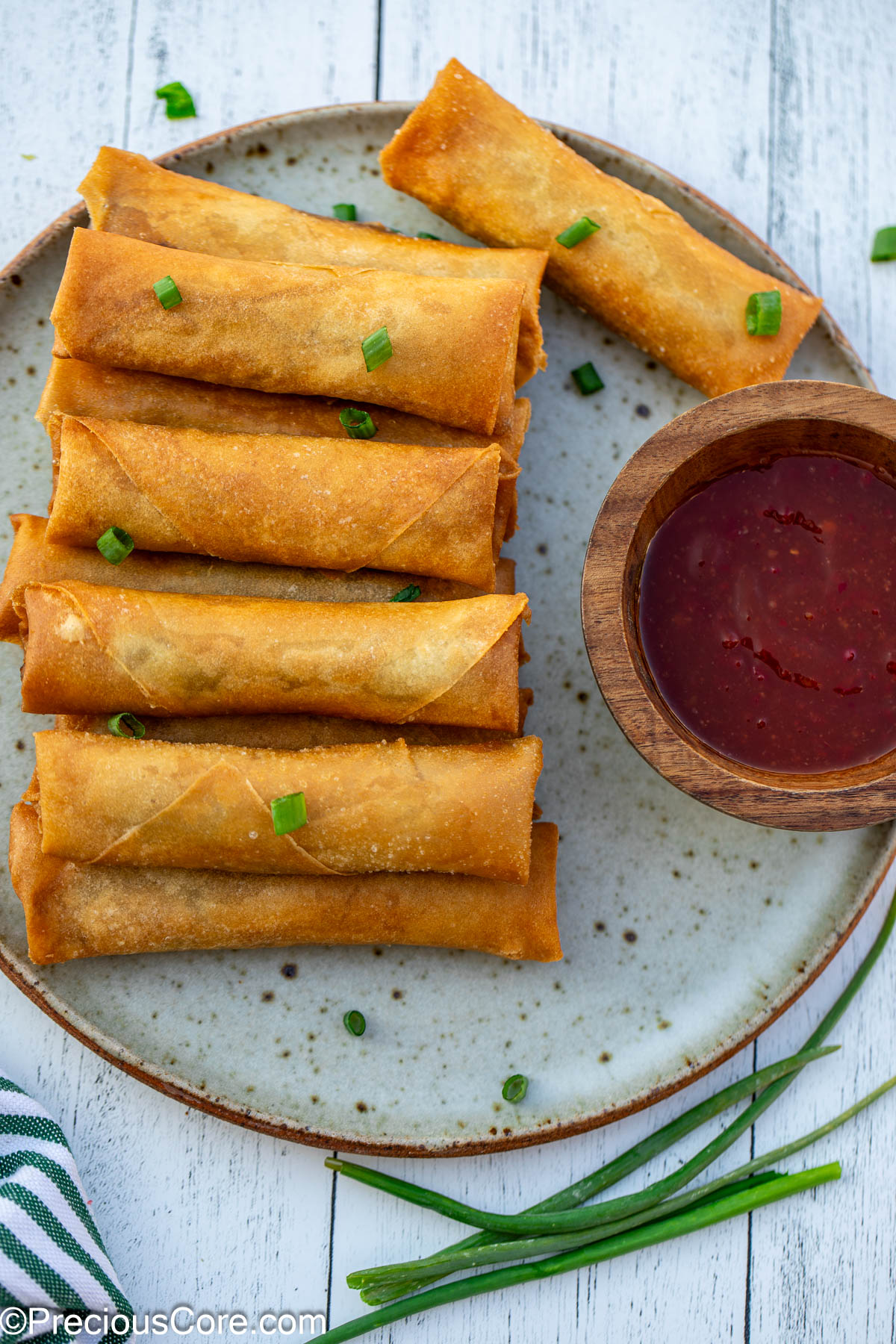 Golden brown spring rolls on a plate, with a bowl of dipping sauce.