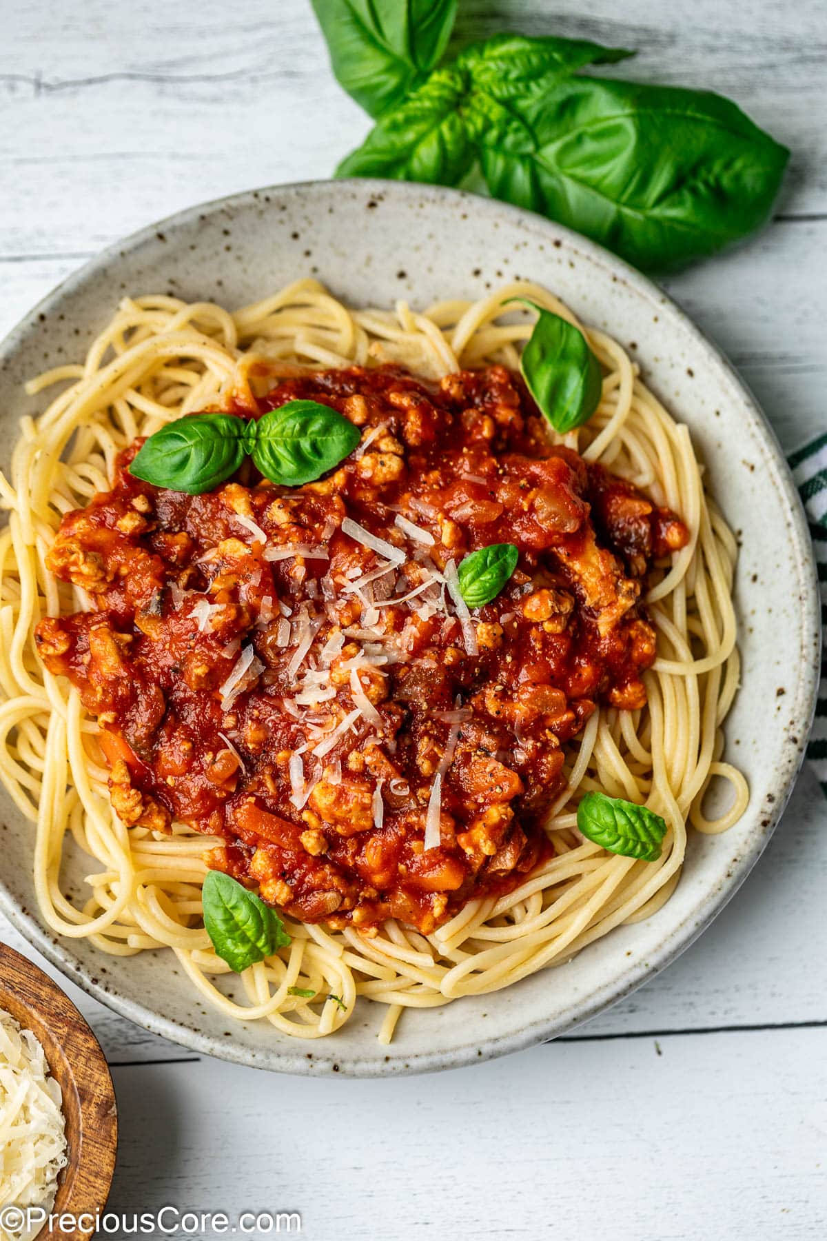 A bowl of spaghetti topped with red sauce, parmesan, and basil leaves.