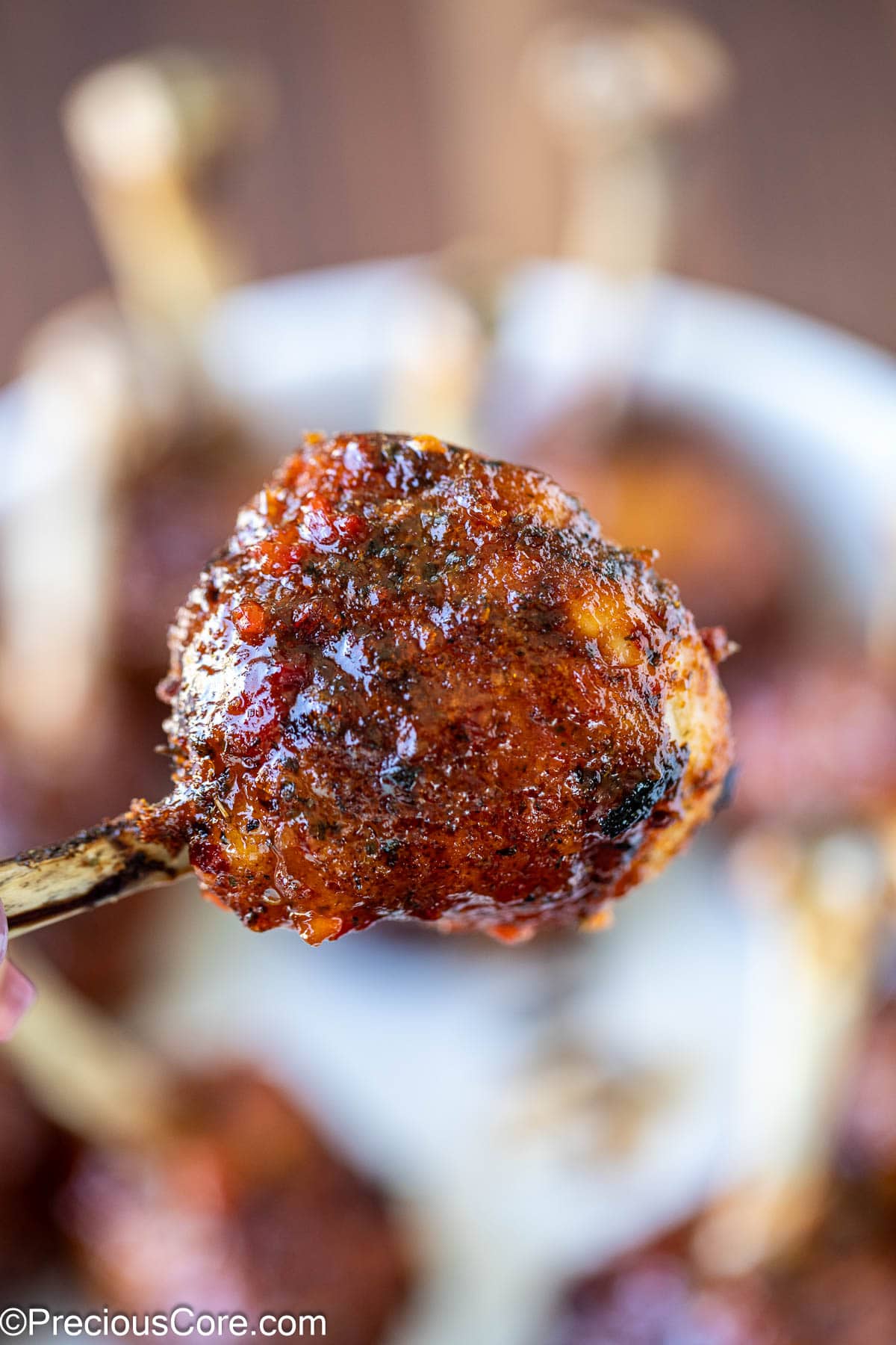 Close-up view of a chicken drumstick lollipop with sauce.