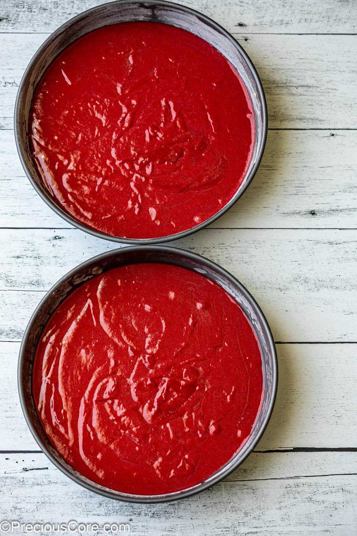 Red cake batter in 9-inch cake pans.