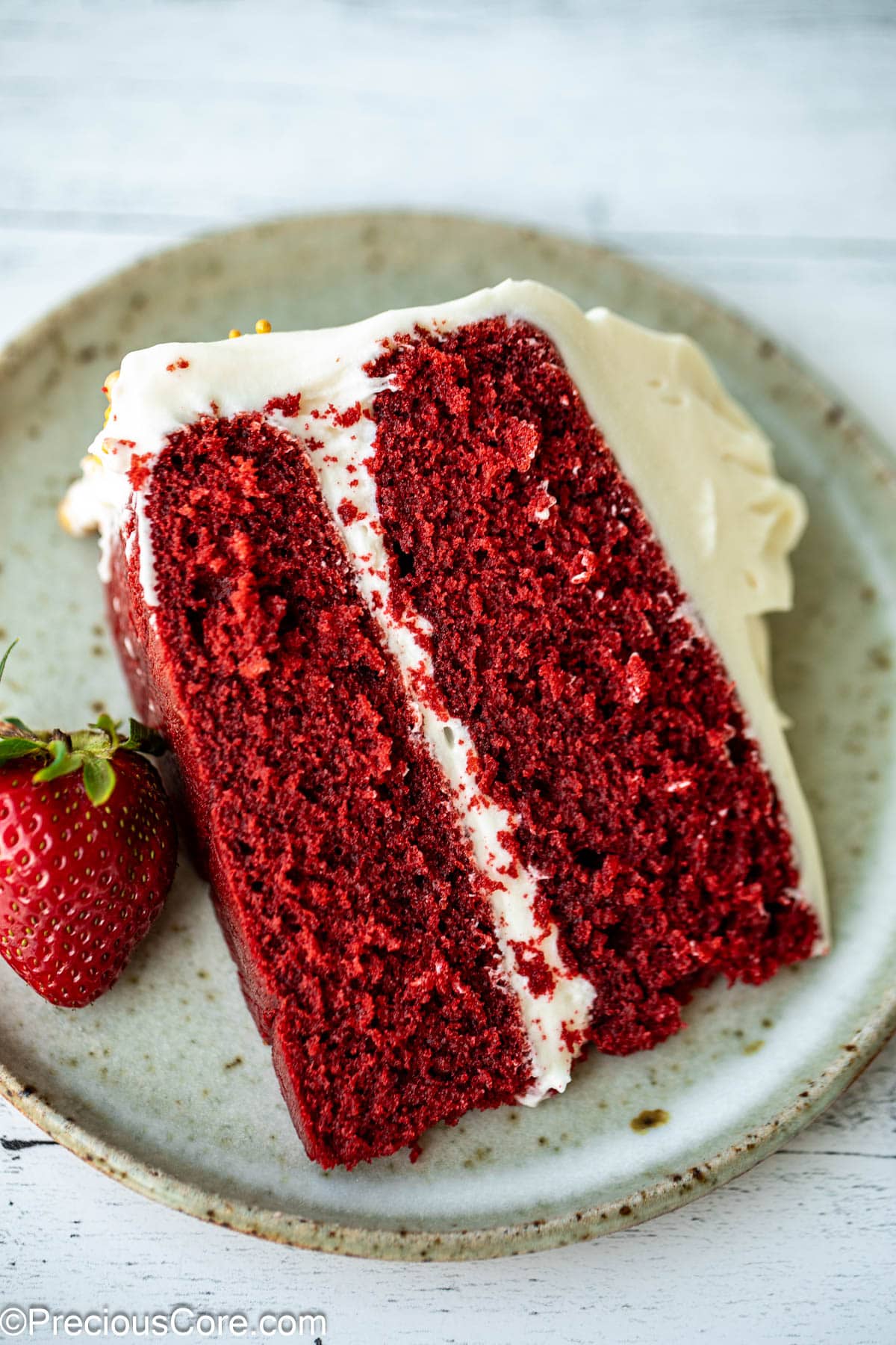 Slice of red velvet cake without buttermilk with strawberry on the side.