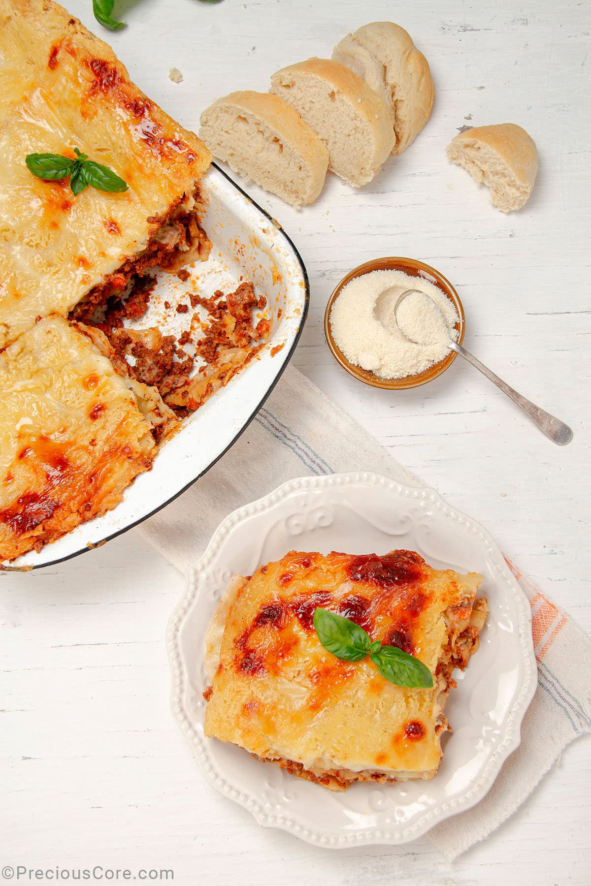 Slice of Lasagna on a plate with a bowl of freshly baked lasagna on the side.