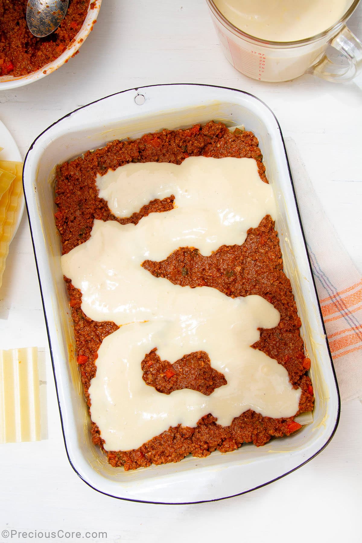 Béchamel sauce over meat sauce in a baking dish.