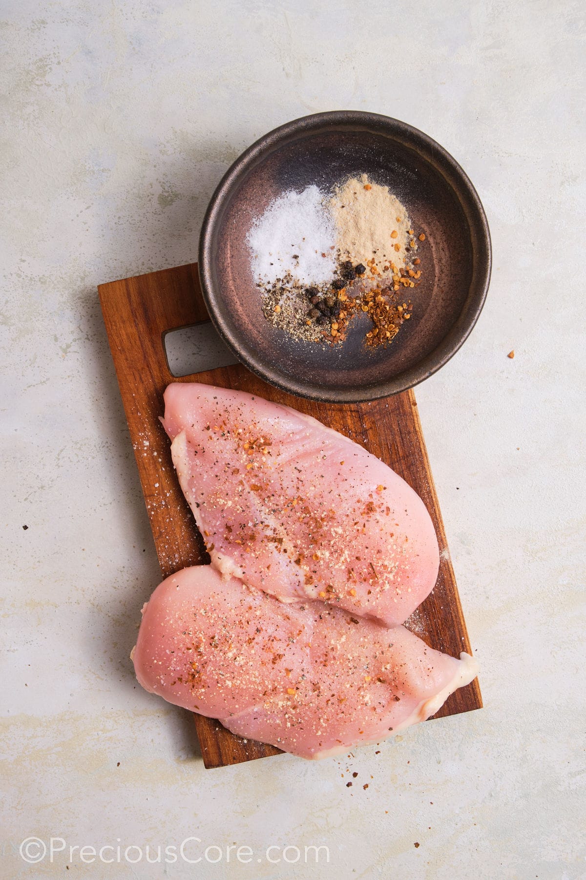 Seasoning chicken breasts on a chopping board.