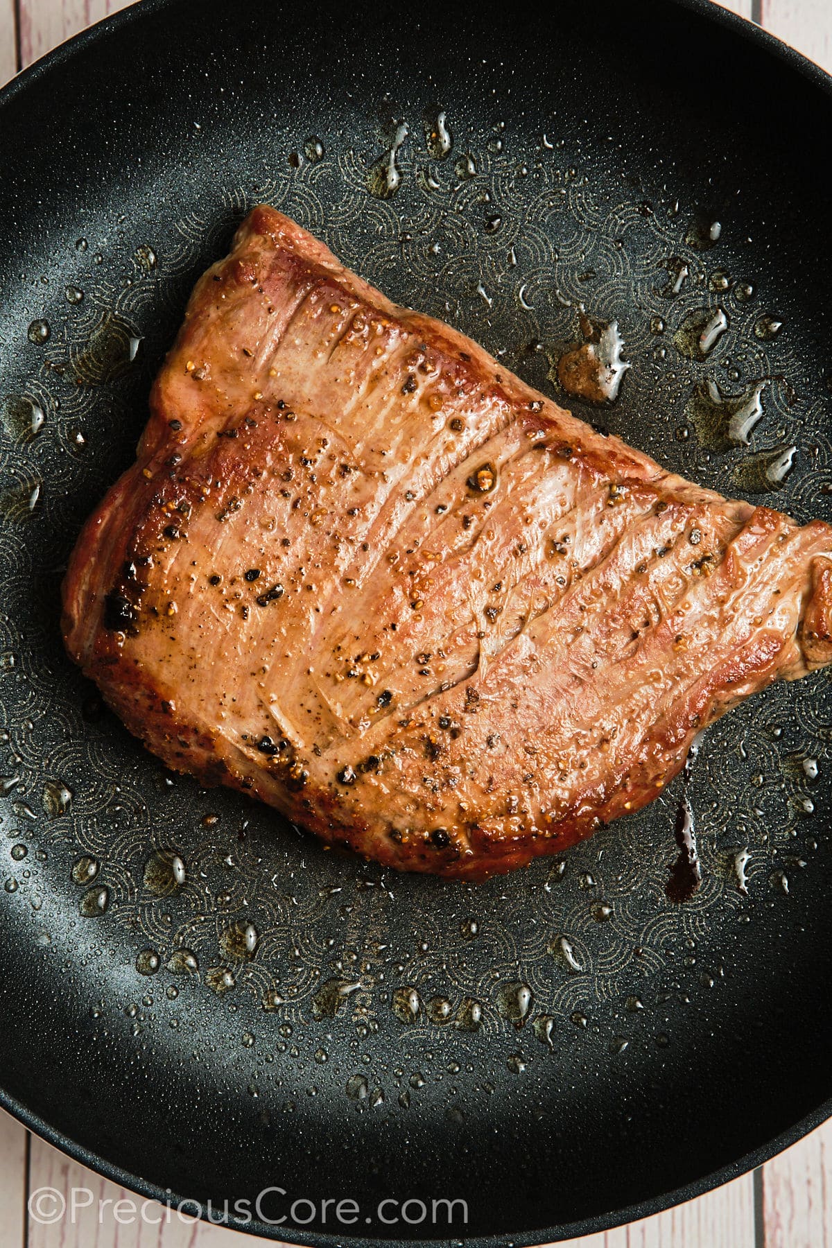 Searing a piece of flank steak in a hot skillet.