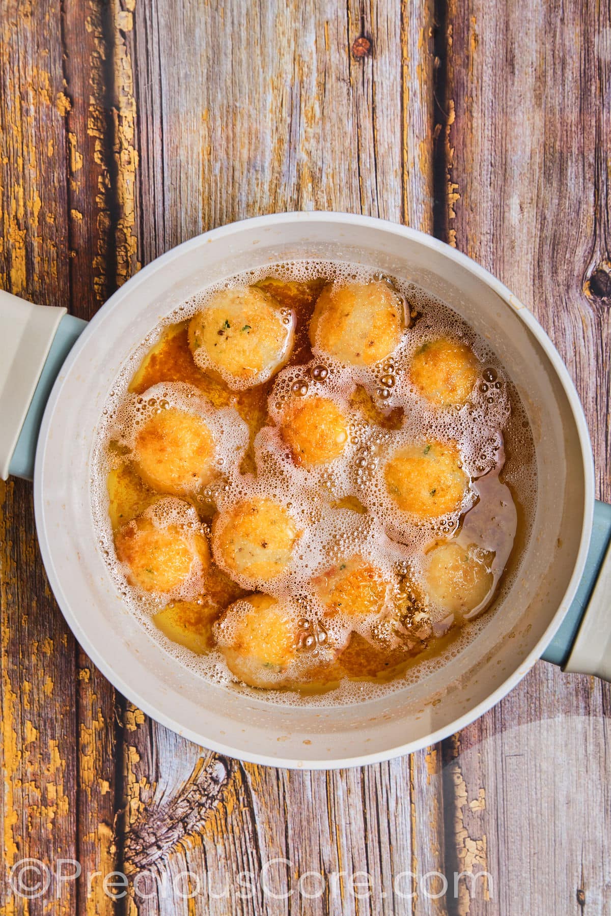 Potato cheese balls deep frying in oil.