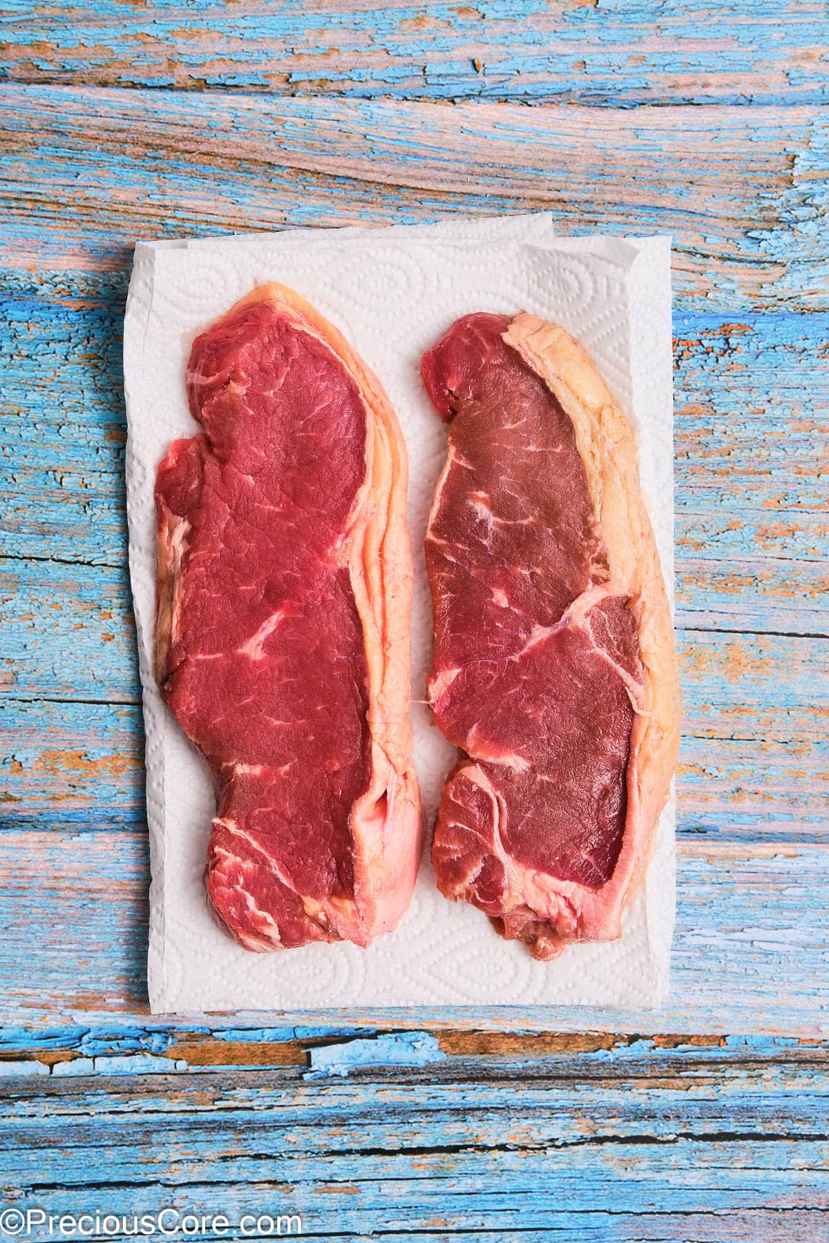 Two ribeye steaks on paper towels.