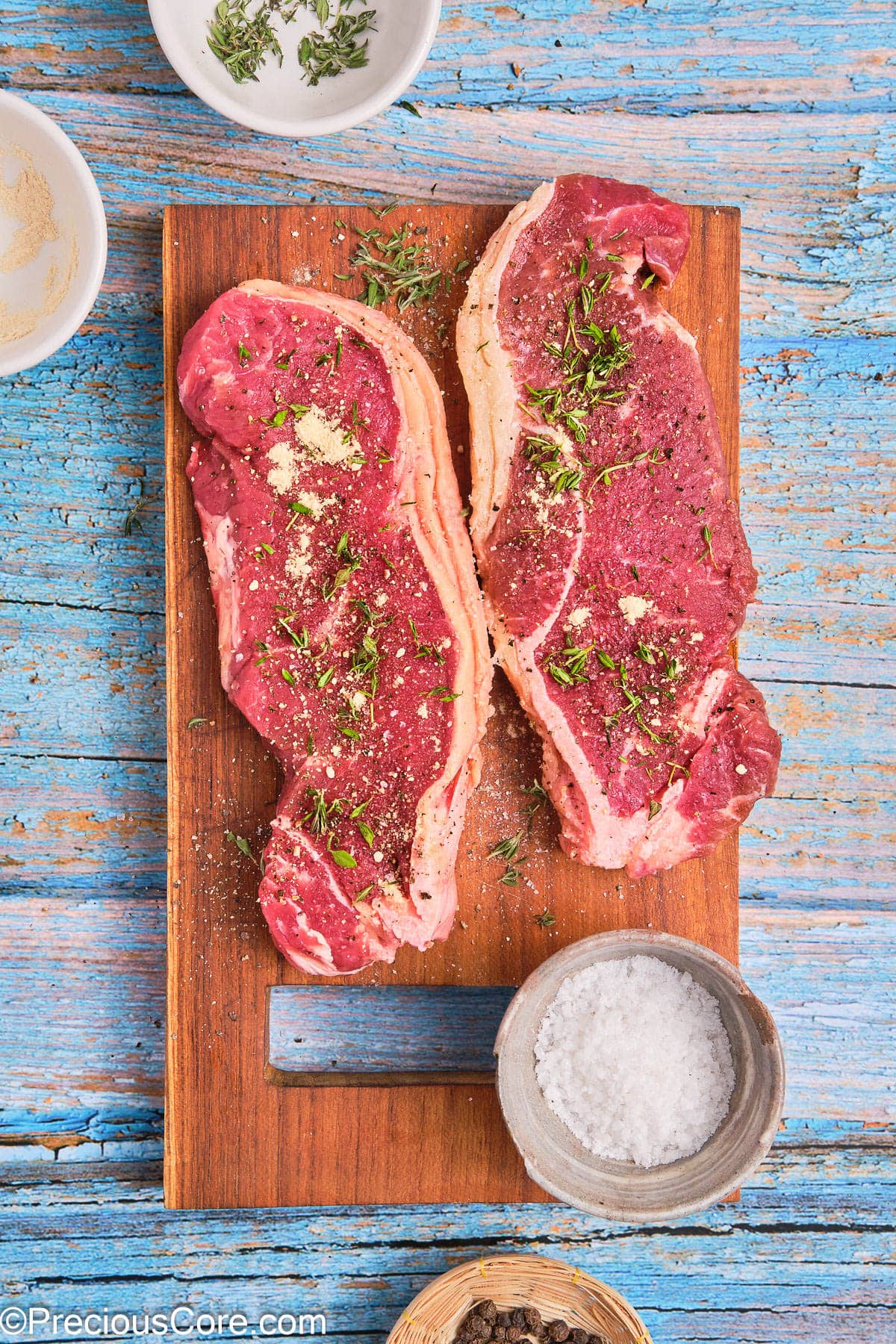 Two seasoned ribeye steaks on a chopping board.