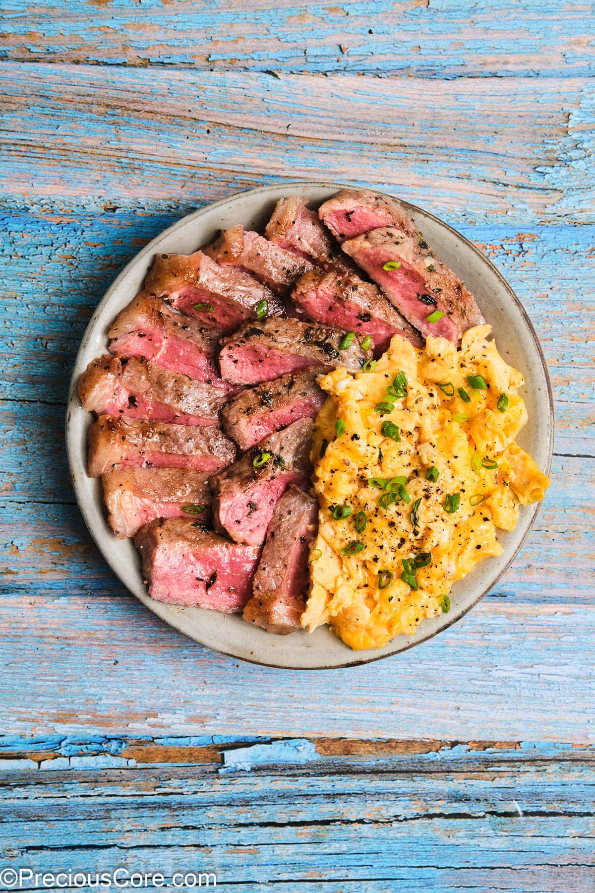 A plate of sliced steak with soft scrambled eggs.