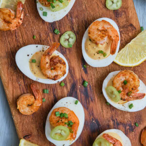 Deviled eggs with Cajun shrimp on a chopping board.