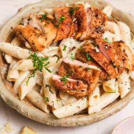 Creamy pasta in a bowl, topped with pan-seared chicken.