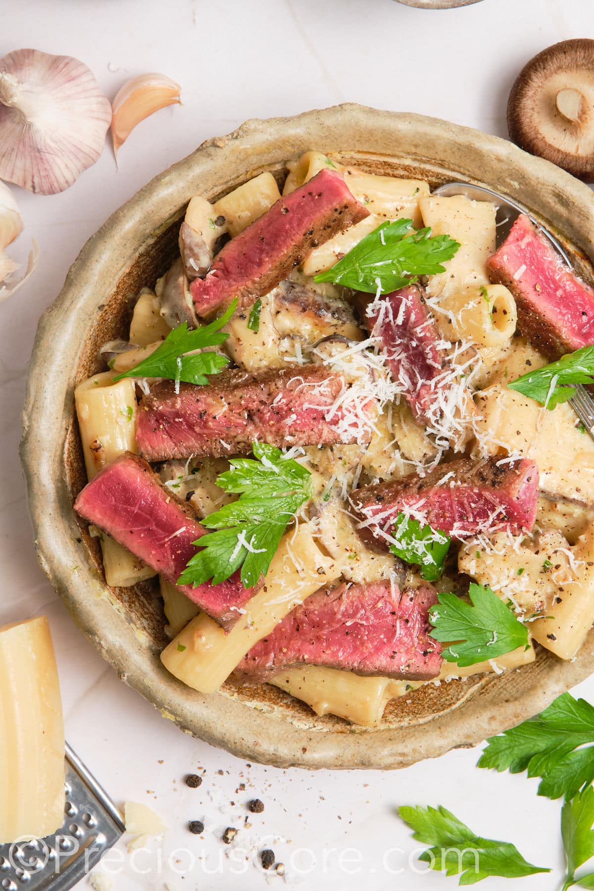 Creamy pasta in a bowl topped with juicy steak.