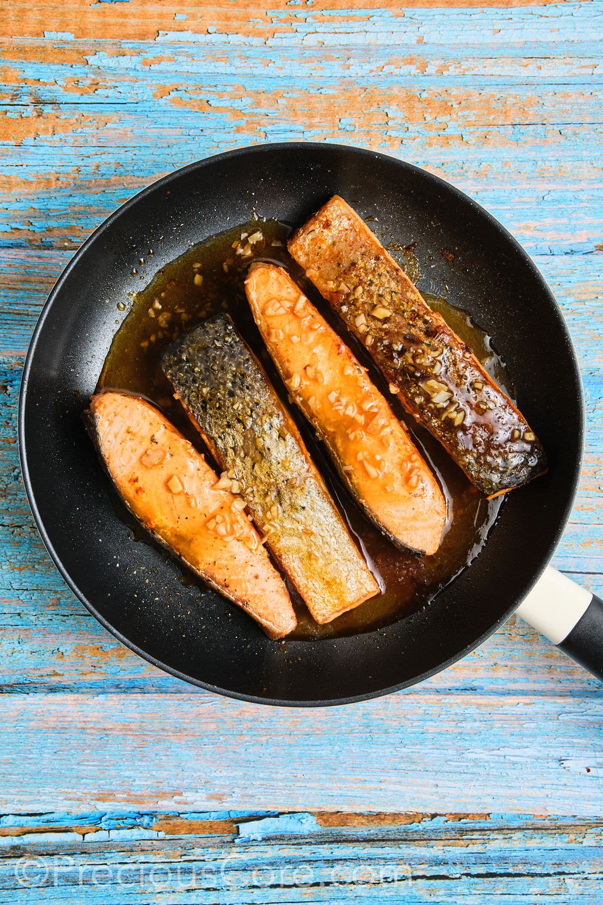 Salmon in skillet simmered in honey butter sauce.