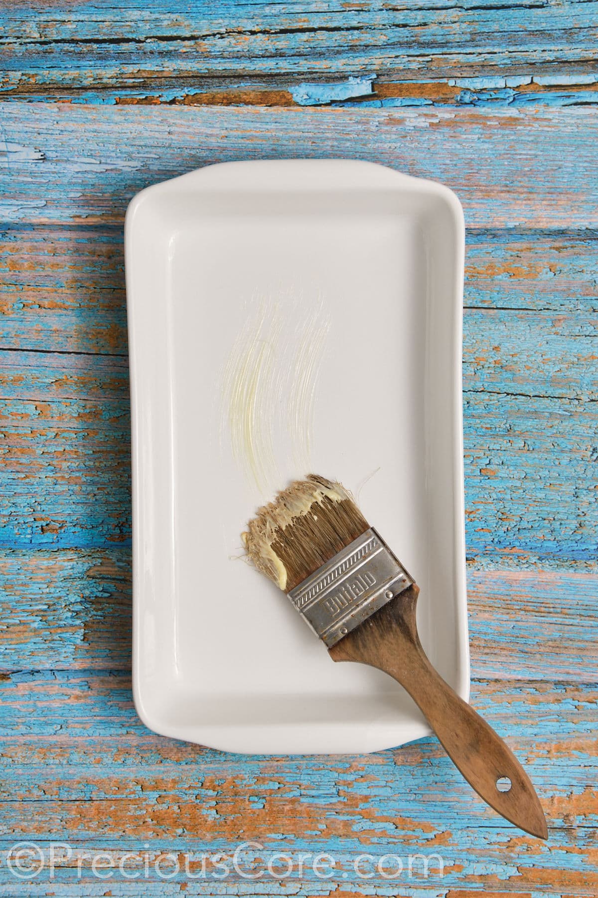 Brushing a casserole dish with softened butter.