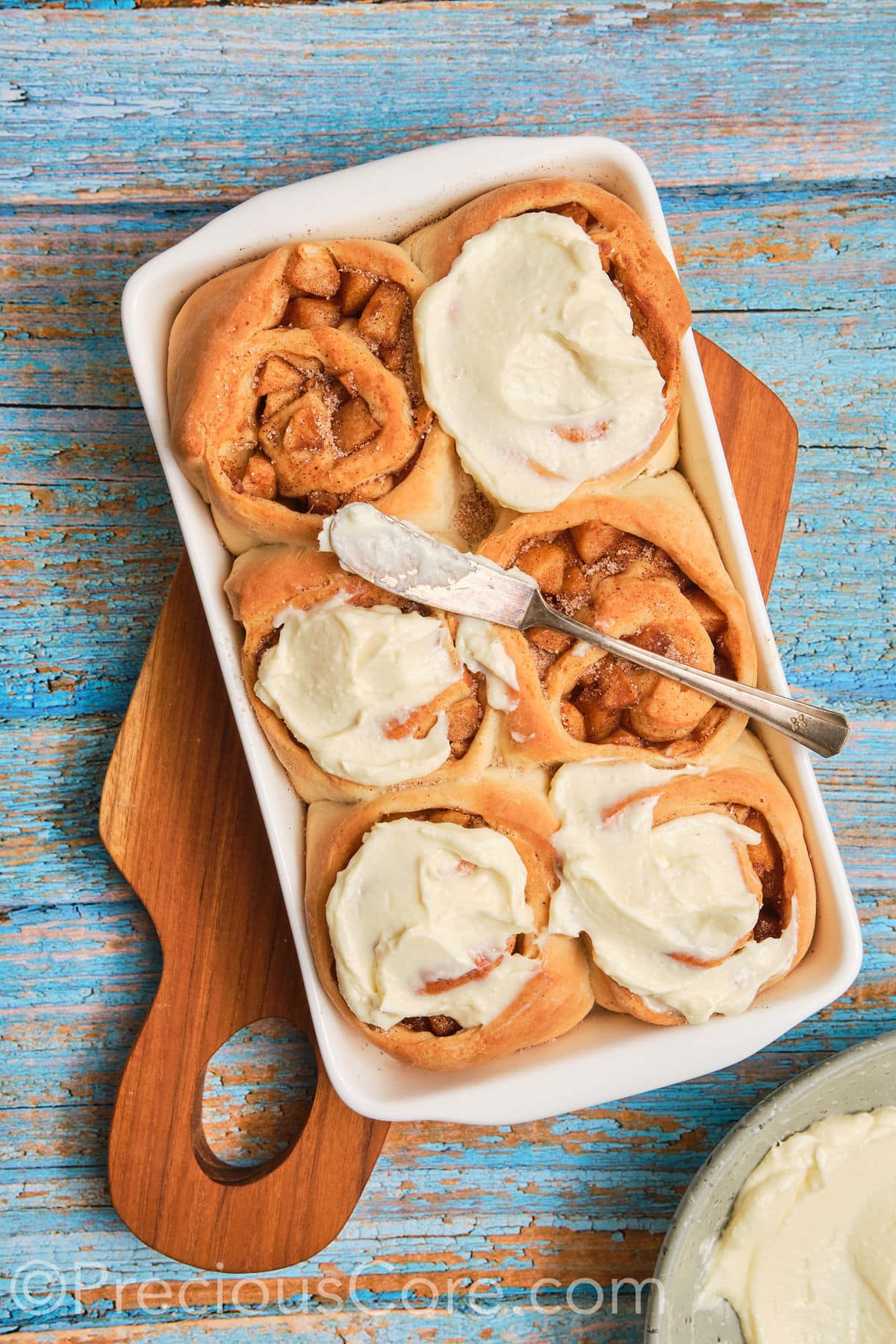 Spreading cream cheese frosting on apple cinnamon rolls.