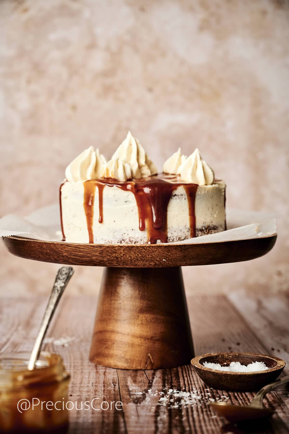 Cake covered in white frosting and caramel drip on a cake stand.