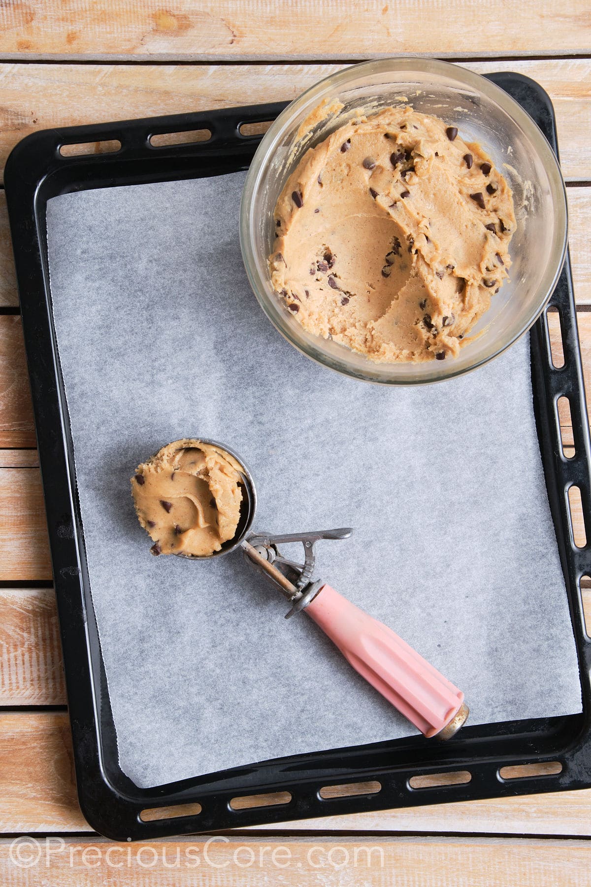 A scoop filled with the cookie dough, placed on a lined baking sheet