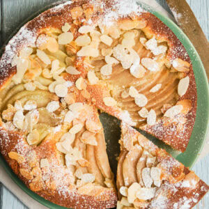 Italian pear almond cake on a plate with a slice cut out.