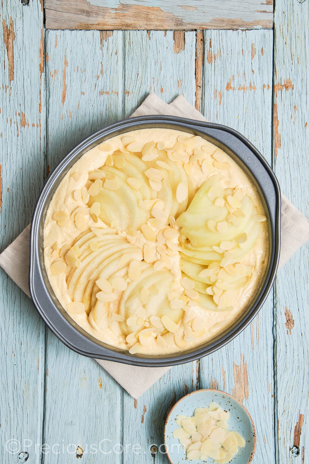 cake batter topped with sliced pears and almond flakes. 