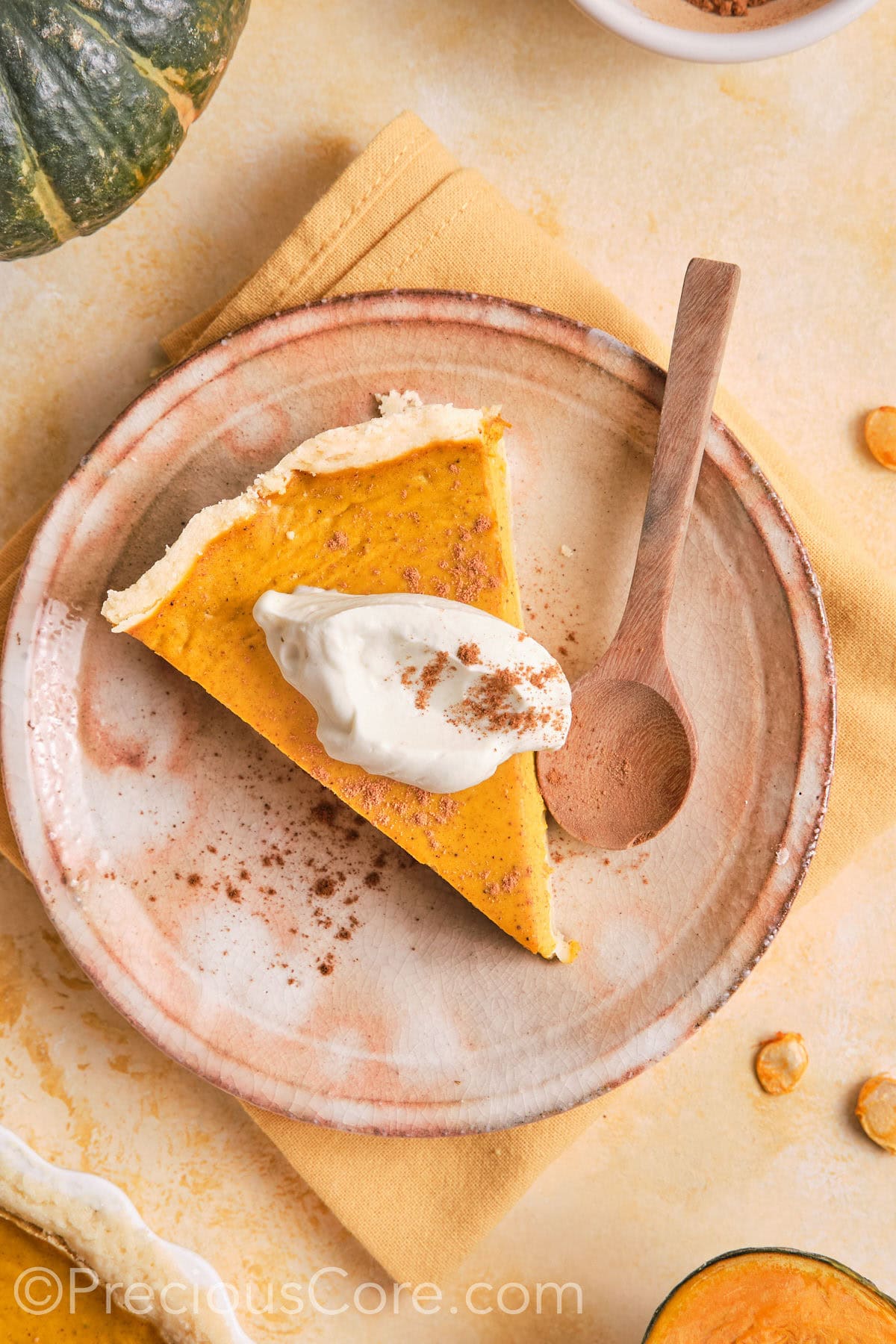 Pumpkin pie on a plate topped with cream and cinnamon.