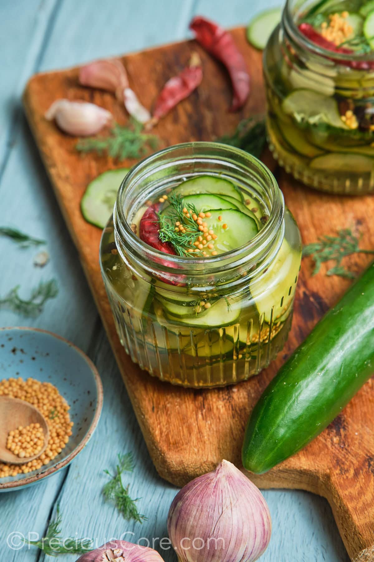 Wide shot showing cucumbers in a jar and other ingredients all around it.