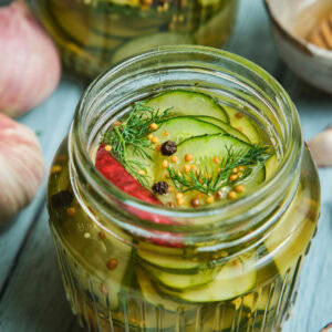 Quick pickled cucumbers in a mason jar with peppercorns on top.