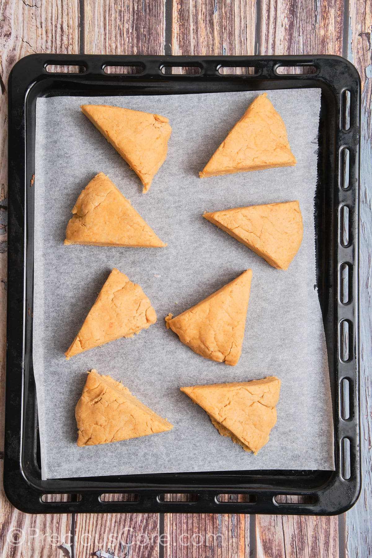 Triangles of unbaked scones placed on parchment paper.