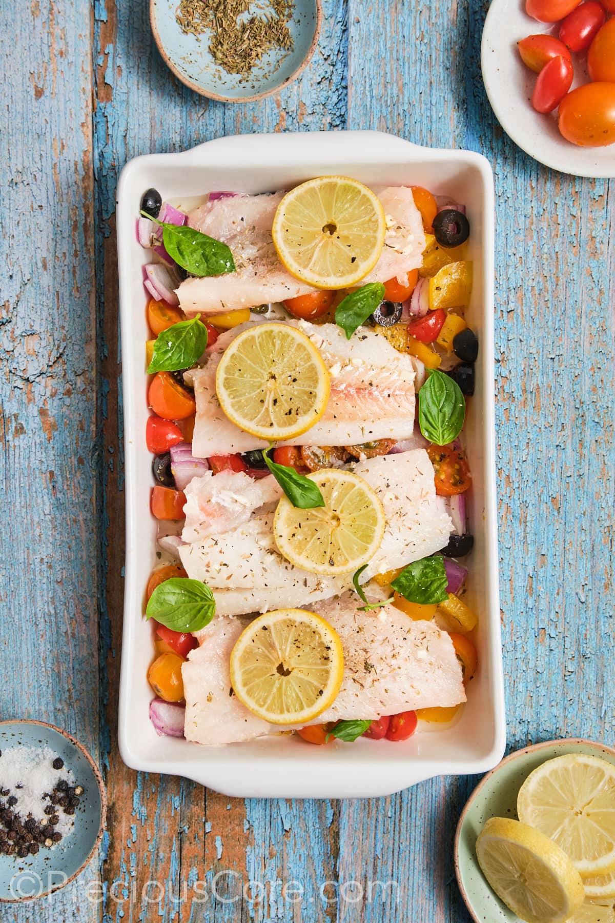 Baking dish filled with chopped veggies, marinated fish and lemon slices. 