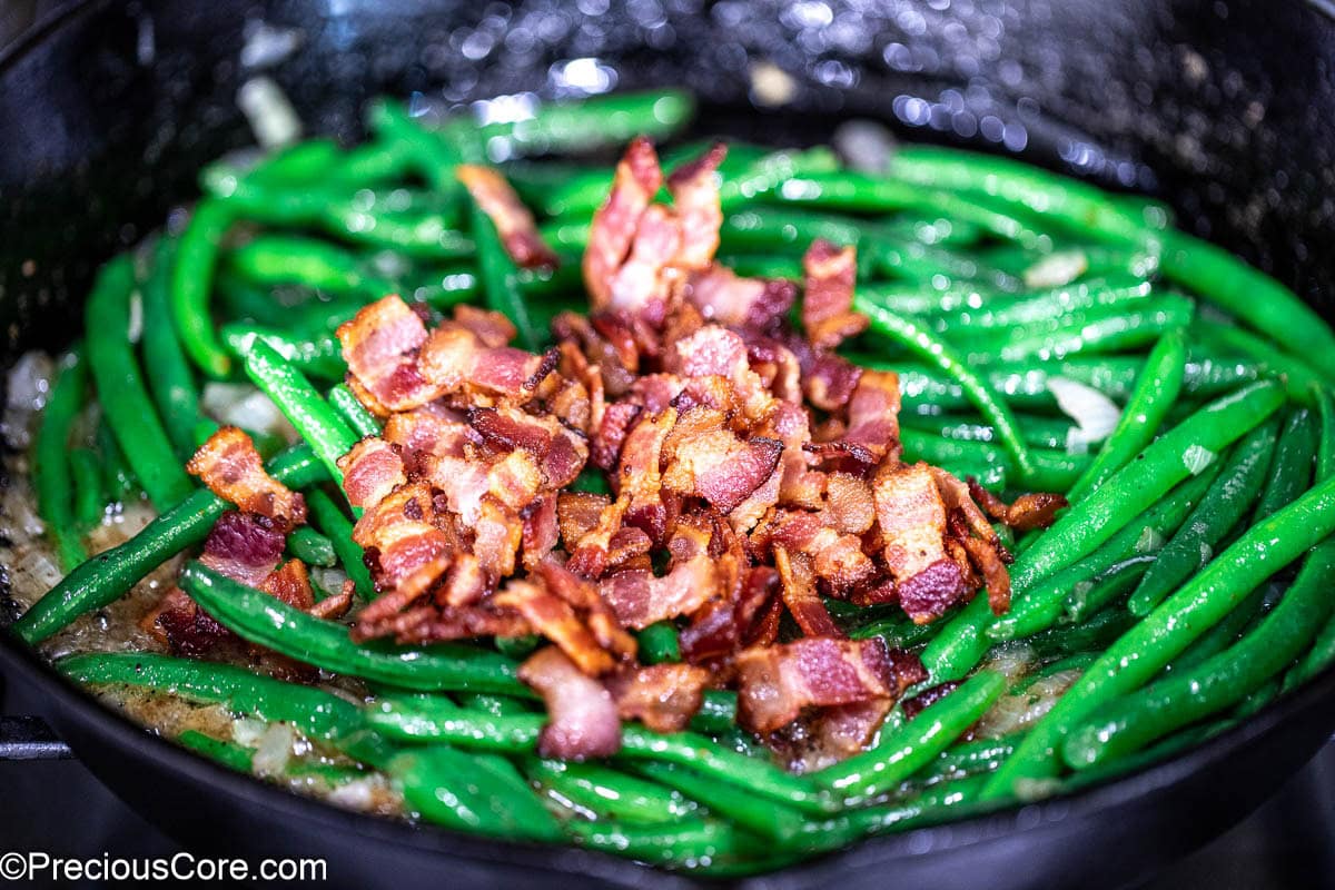 Crispy bacon over green beans in skillet.